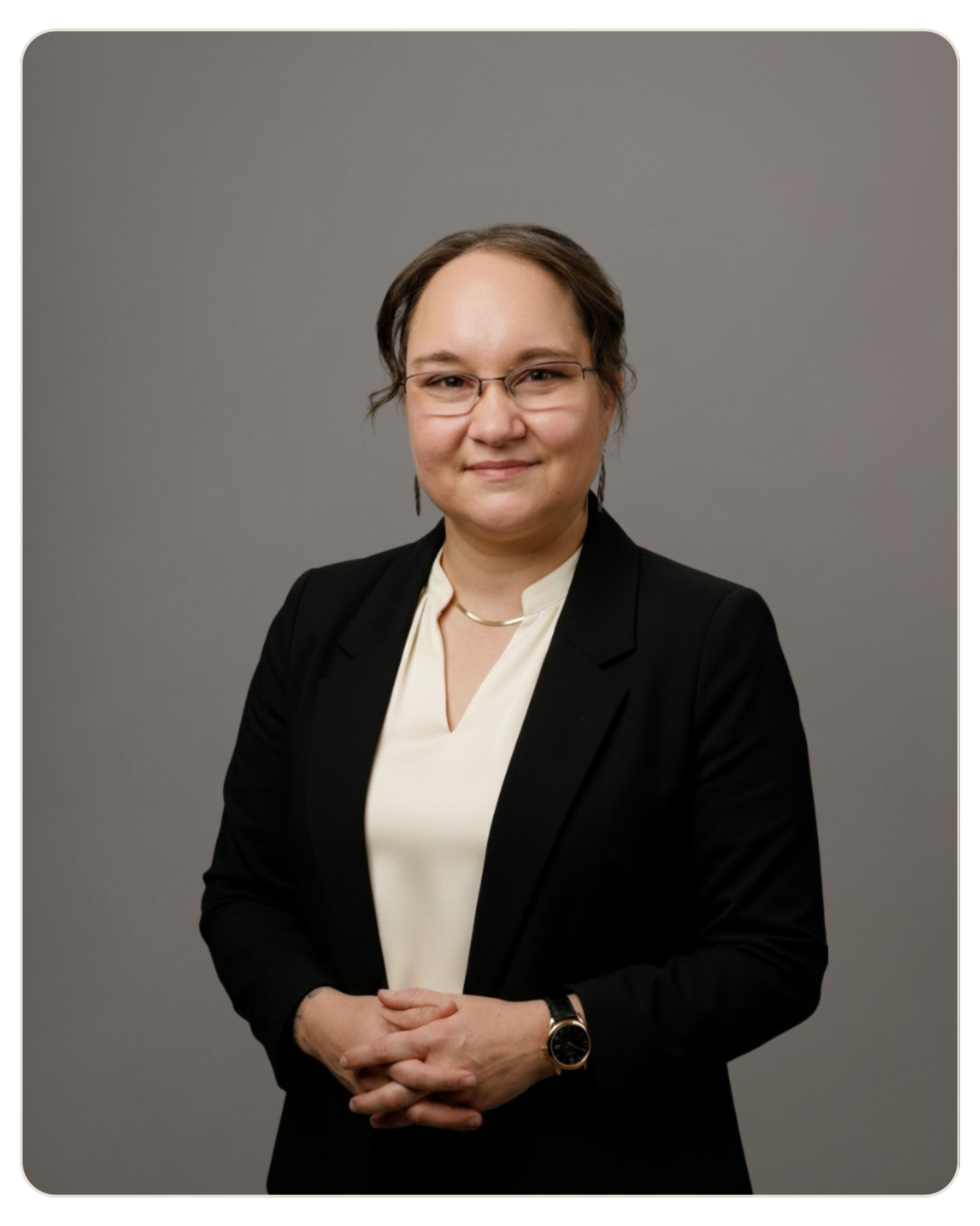 Teri Wilder Professional woman in a black blazer and cream blouse, wearing glasses, with hands folded in front.
